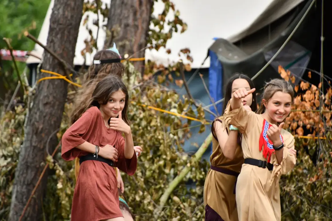 Dziewczynki w strojach indiańskich na scout camp poznań. Jedna pokazuje kciuk w górę, inne pozdrawiają.