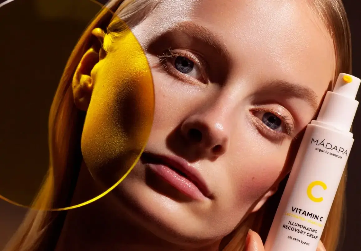 Strahlende Haut dank Vitamin C Skin Care. Eine Frau hält eine Flasche MÁDARA Illuminating Recovery Cream.