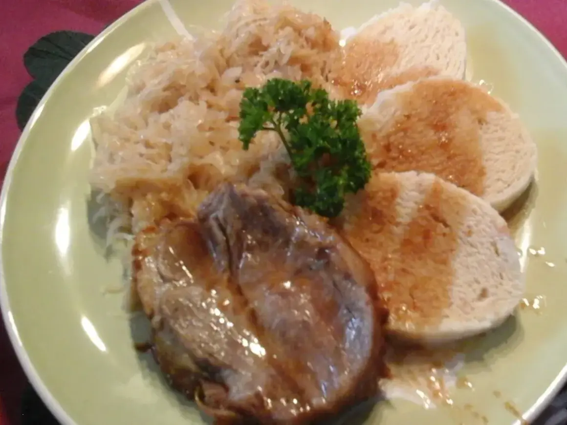 Ein Teller mit tschechischem Schweinebraten, Sauerkraut und Knödeln, garniert mit Petersilie.