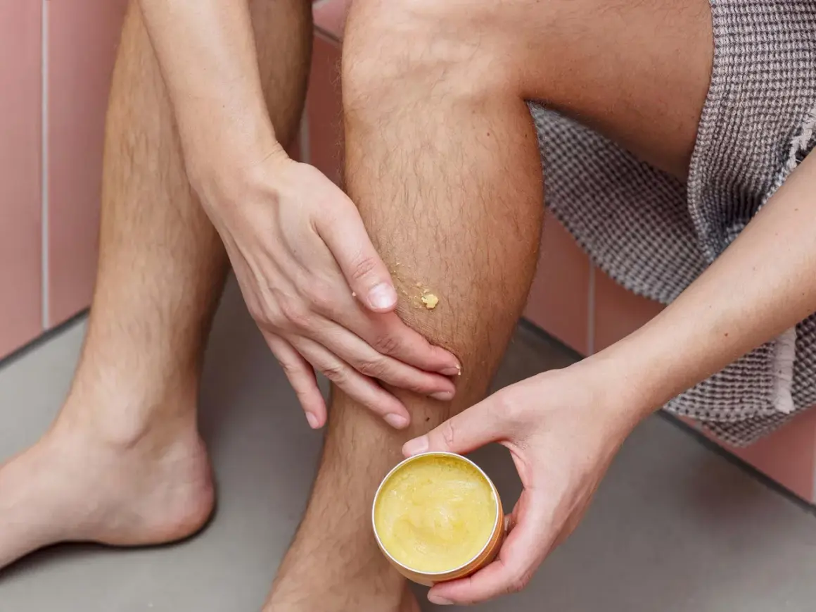 Hände tragen eine gelbe Salbe auf ein Bein auf. Manche glauben, sheabutter trocknet haut aus, aber diese Salbe spendet Feuchtigkeit.