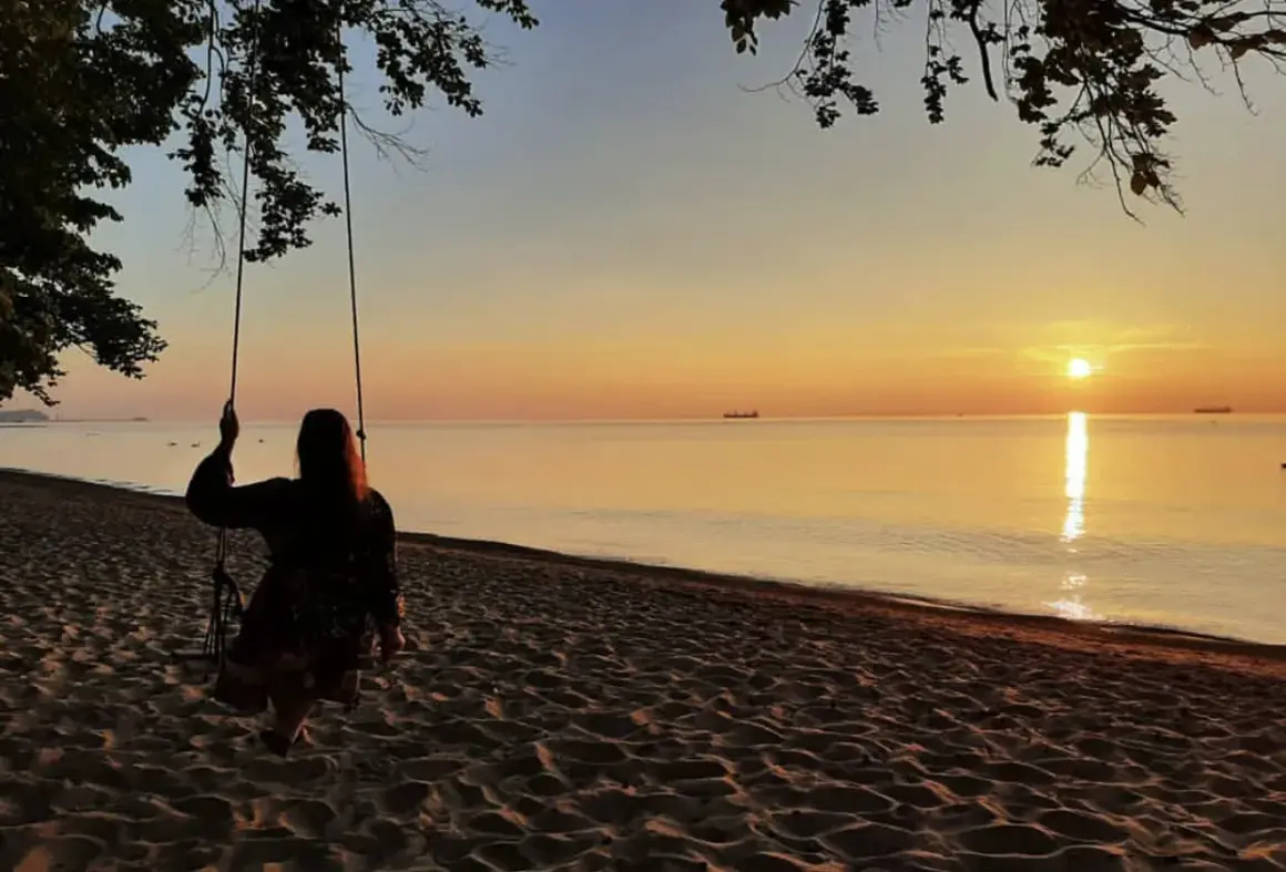 Zachód słońca nad morzem, dziewczyna na huśtawce na plaży.