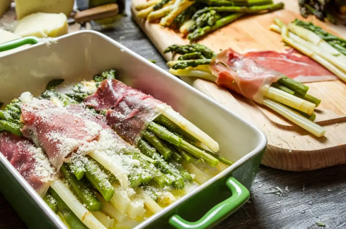 Zielone i białe szparagi w szynce na zimno, posypane parmezanem, gotowe do pieczenia.