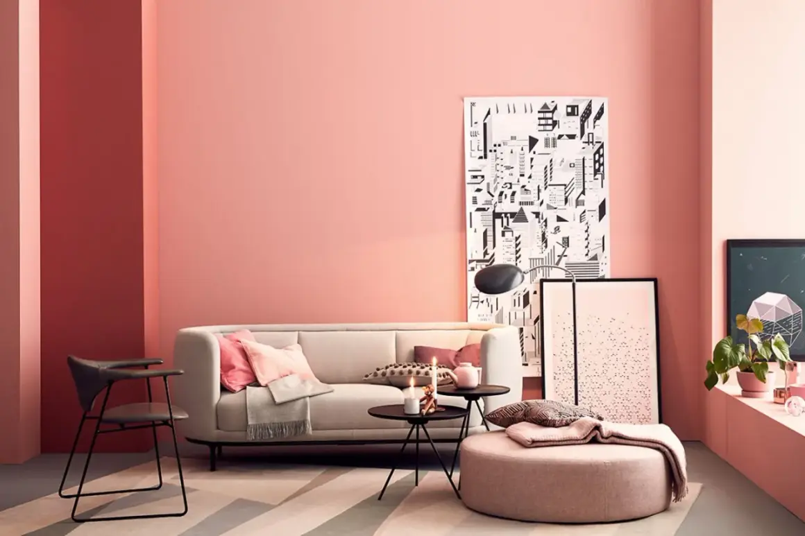 Gemütliches Wohnzimmer mit einer rosa Wand, einem hellen Sofa, Kissen und einem runden Hocker.