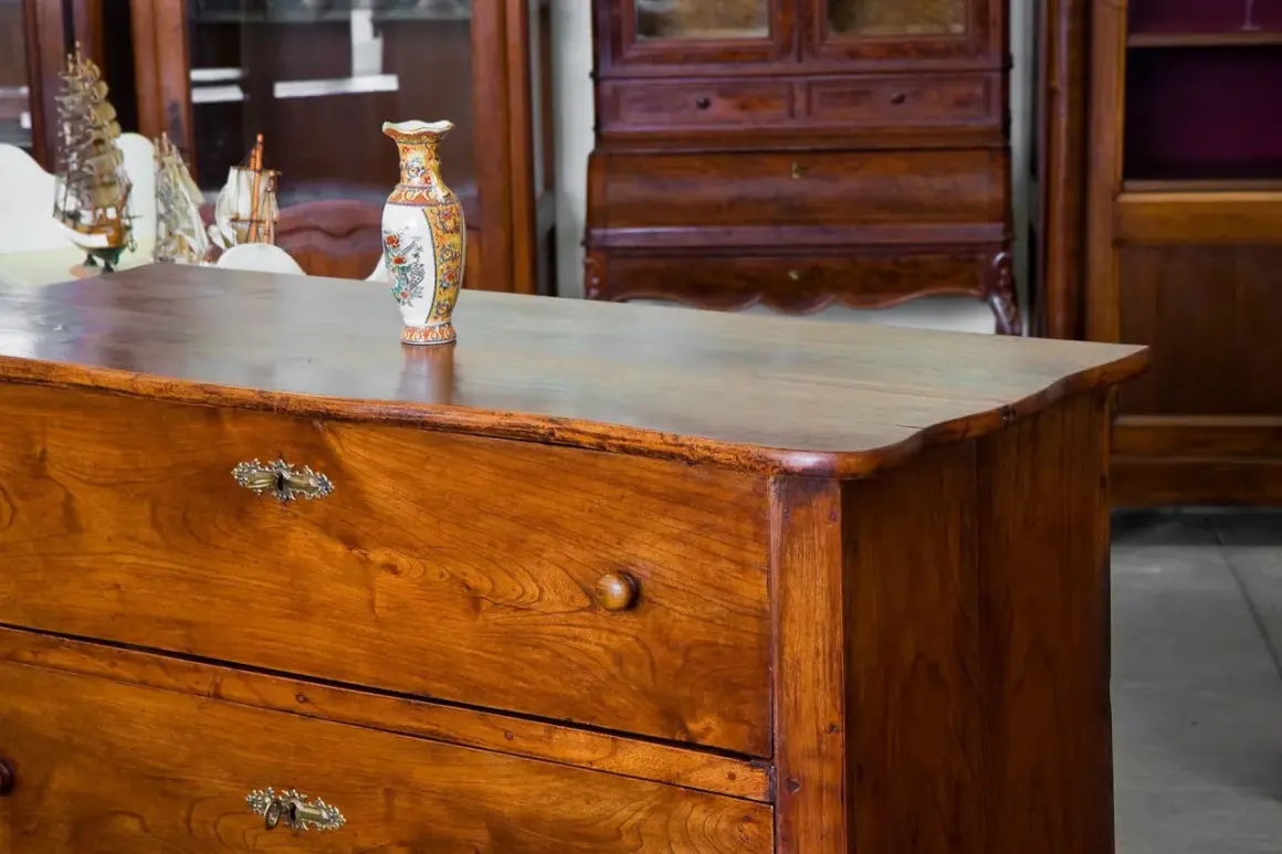 Cassettiera in legno con maniglie antiche e vaso decorato. Un esempio di come antichizzare un mobile per un tocco vintage.