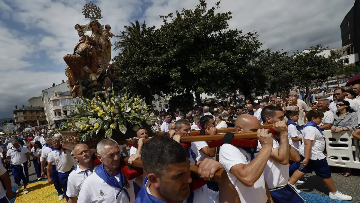 Procesión de la Virgen en las fiestas del Carmen de Foz. Hombres portan la imagen adornada con flores, mientras una multitud observa.