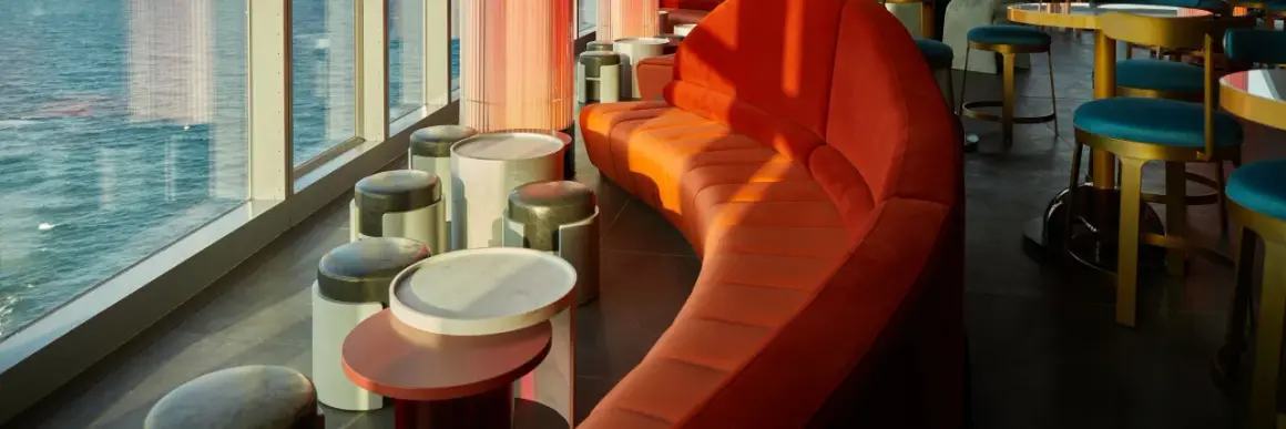 Arredamento moderno con divano curvo arancione e sgabelli in un w barcelona rooftop bar con vista sul mare.