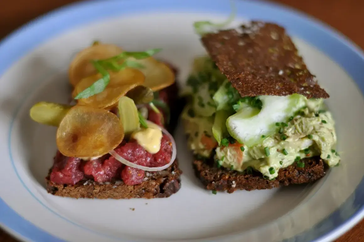 Dos sándwiches abiertos, uno con tartar de ternera y patatas fritas, otro con ensalada de pollo y pepino. Comida típica de Dinamarca.