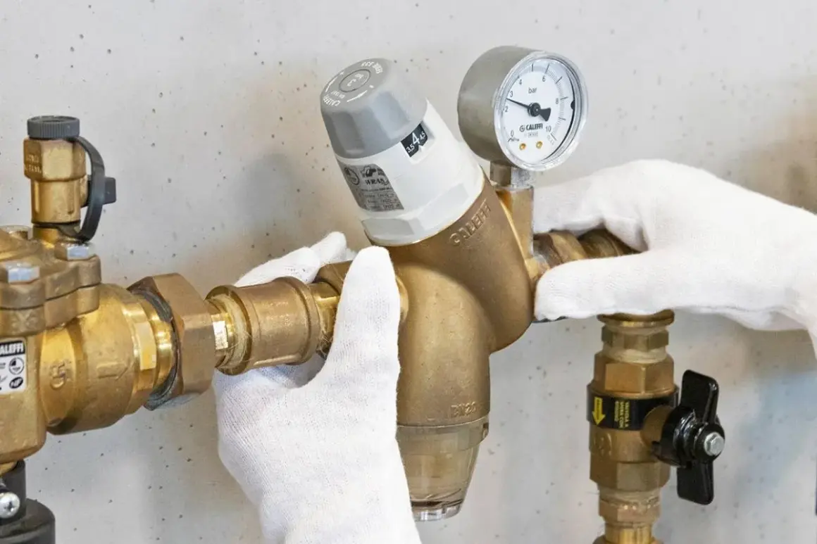Mani guantate regolano un riduttore di pressione con manometro, mostrando come si regola la pressione dell'acqua.