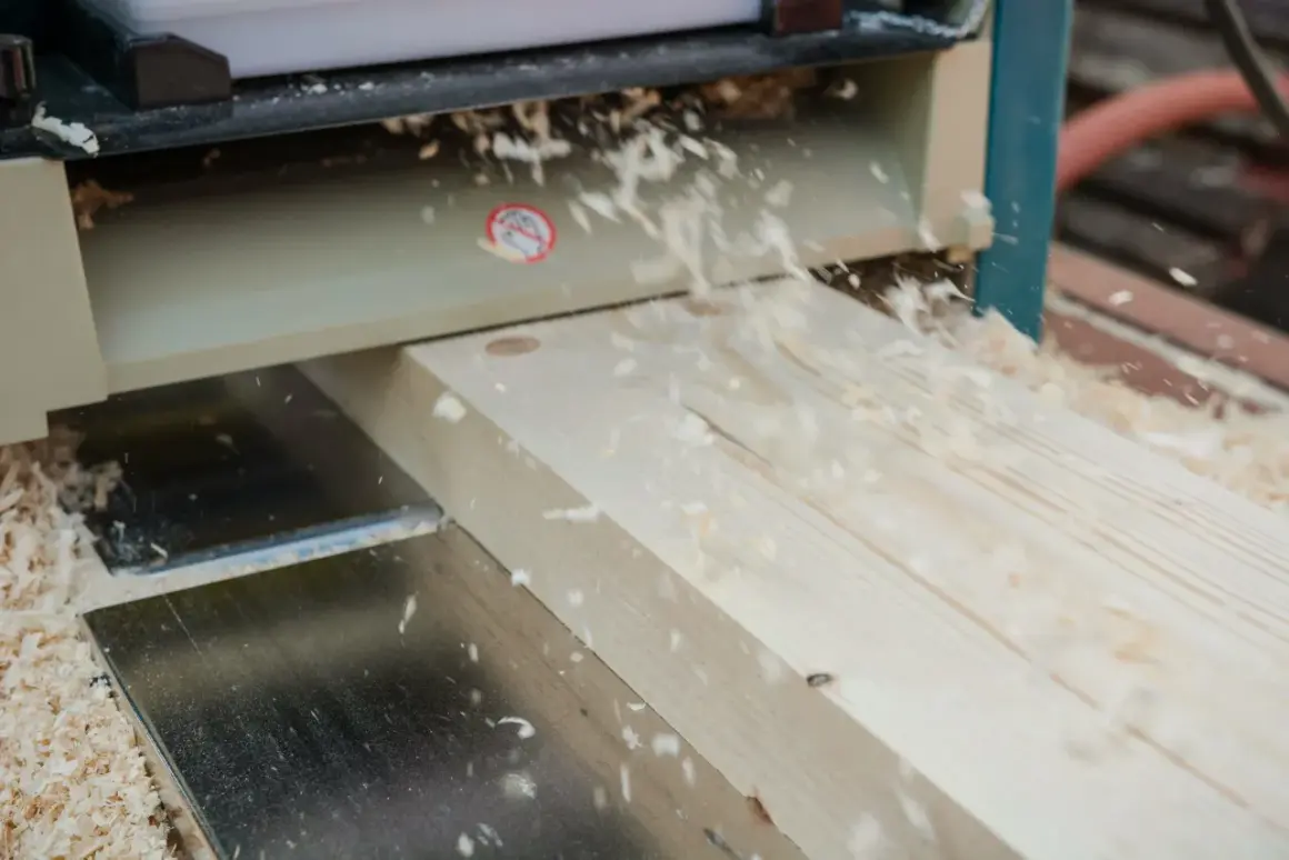 Le bois est raboté avec précision par la dégau rabot, créant une surface lisse et des copeaux fins qui volent dans l'air.