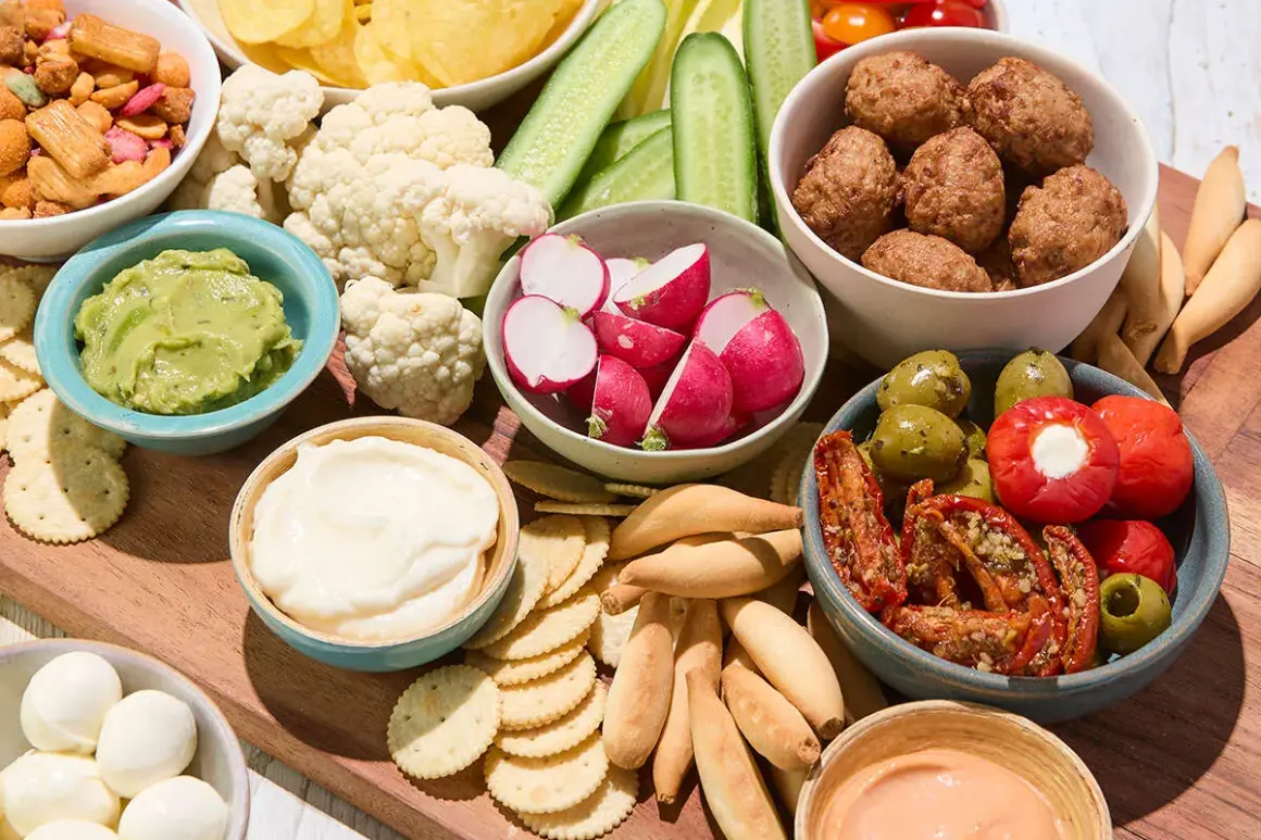 Un plateau garni pour un apéro d'été : boulettes, crudités, guacamole, fromages, olives et tomates séchées.