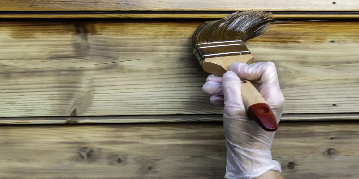 Application d'une lasure sur un bardage en bois, montrant la différence entre lasure et peinture. La lasure pénètre le bois, la peinture le recouvre.