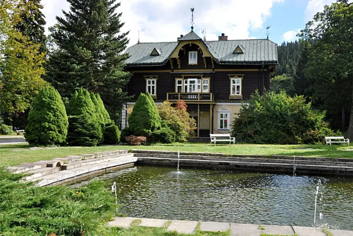 Urokliwy dworek w Karlovej Studance z basenem i fontannami, otoczony zielenią.