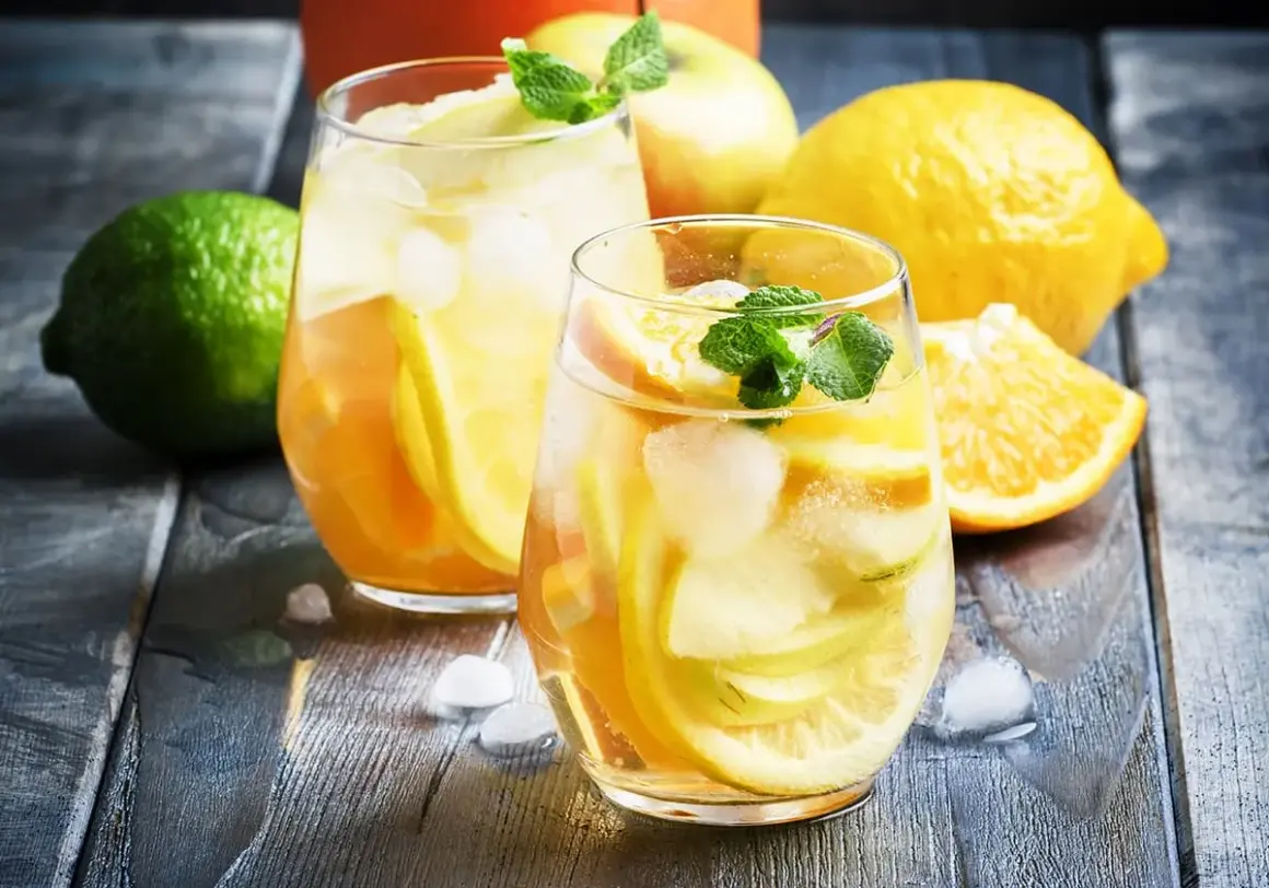 Två glas med uppfriskande vit sangria fyllda med frukt och is. Citroner, äpplen och apelsiner ger en härlig smak.