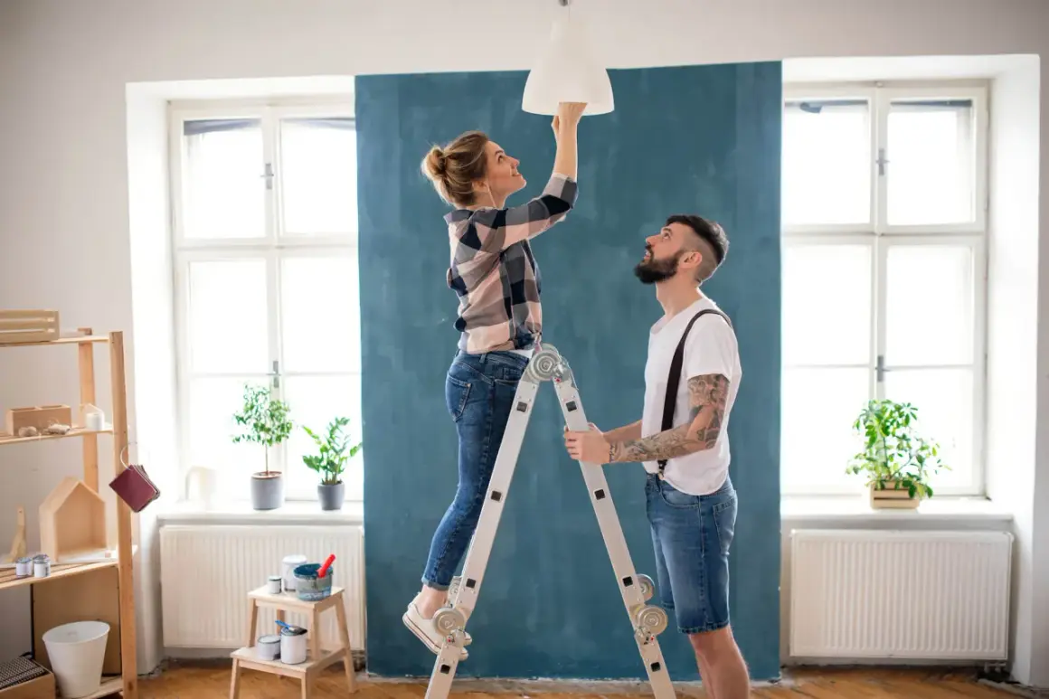 Coppia installa un lampadario, una delle migliorie che aumentano il valore di un immobile.