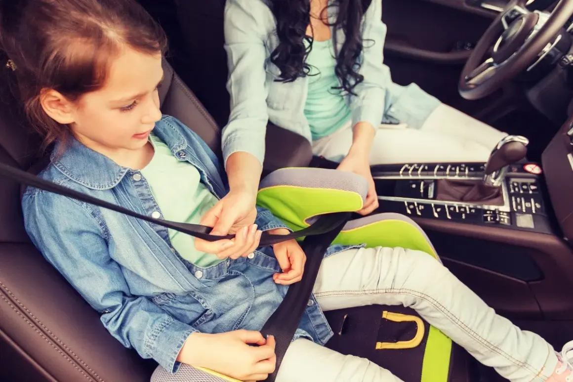 Ein Kind im Kindersitz wird angeschnallt. Die Frage "ab wann darf ein Kind vorne sitzen" ist hier relevant, da sie auf dem Beifahrersitz sitzt.