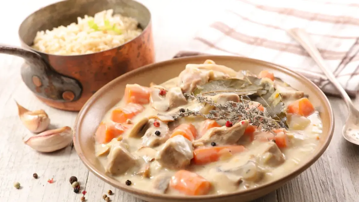 Un delicioso blanquette de ternera con zanahorias y champiñones en una cremosa salsa, servido con arroz blanco.