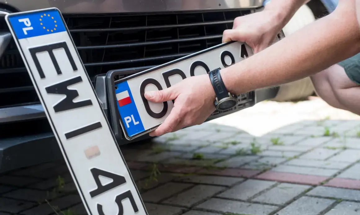 Ręce montują polską tablicę rejestracyjną. Nowe oznaczenie pojazdu gotowe do drogi.
