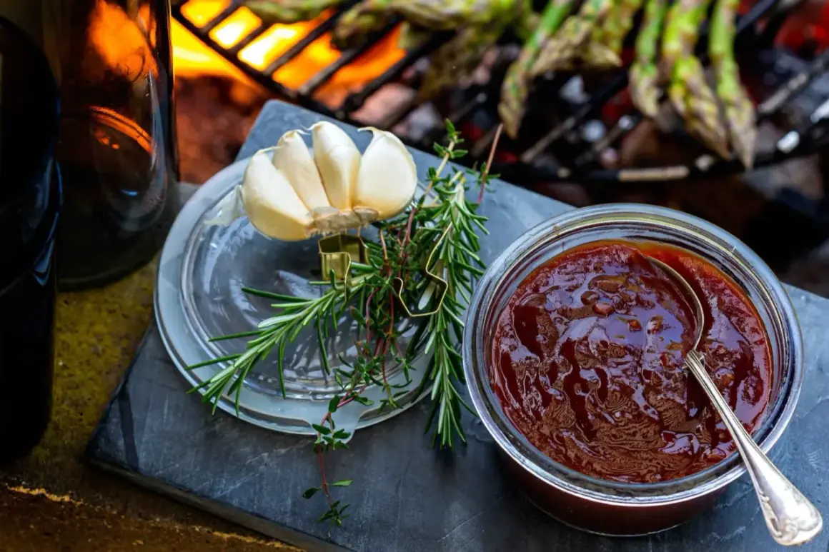 En burk med hemlagad bbq sås, vitlök och färska örter förbereds för grillen där sparris redan ligger på gallret.