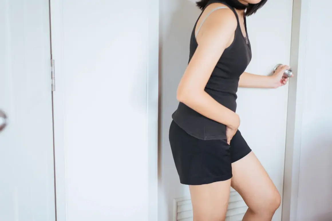 Femme se tenant la main sur le bas-ventre, porte ouverte, ressentant une forte sensation vessie pleine.