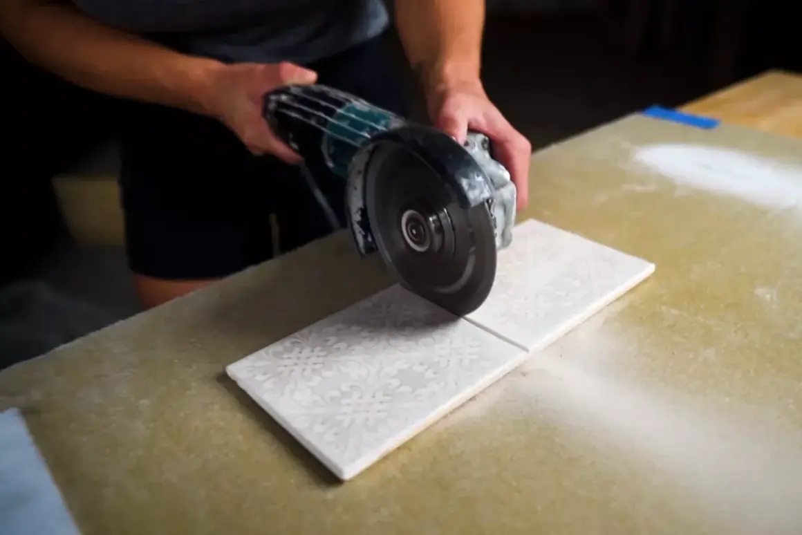 Hands carefully cutting decorative porcelain tile with an angle grinder, creating a clean line.