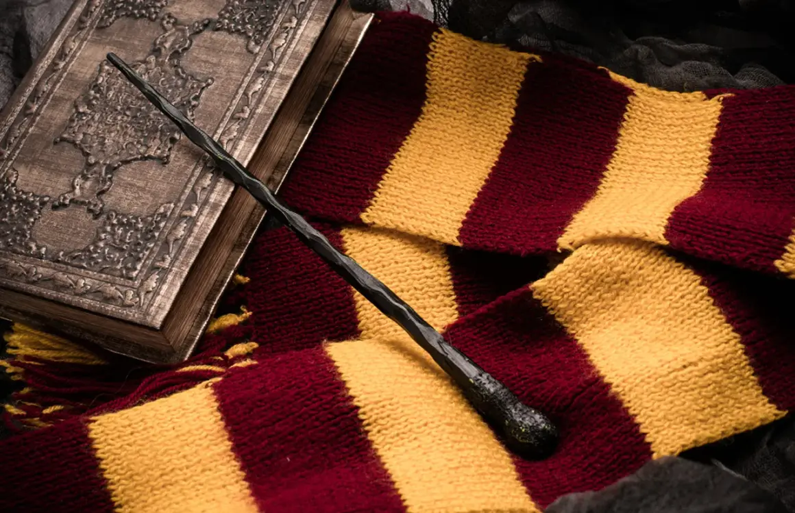 Magiczna różdżka i szalik w barwach Gryffindoru leżą obok ozdobnej księgi, idealne dla fanów szukających książek podobnych do Harrego Pottera.