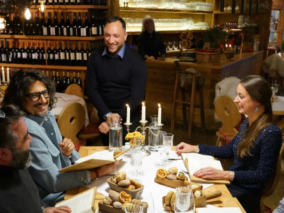 Un gruppo di amici ride a tavola in un ristorante di Milano, tra candele e bottiglie di vino.