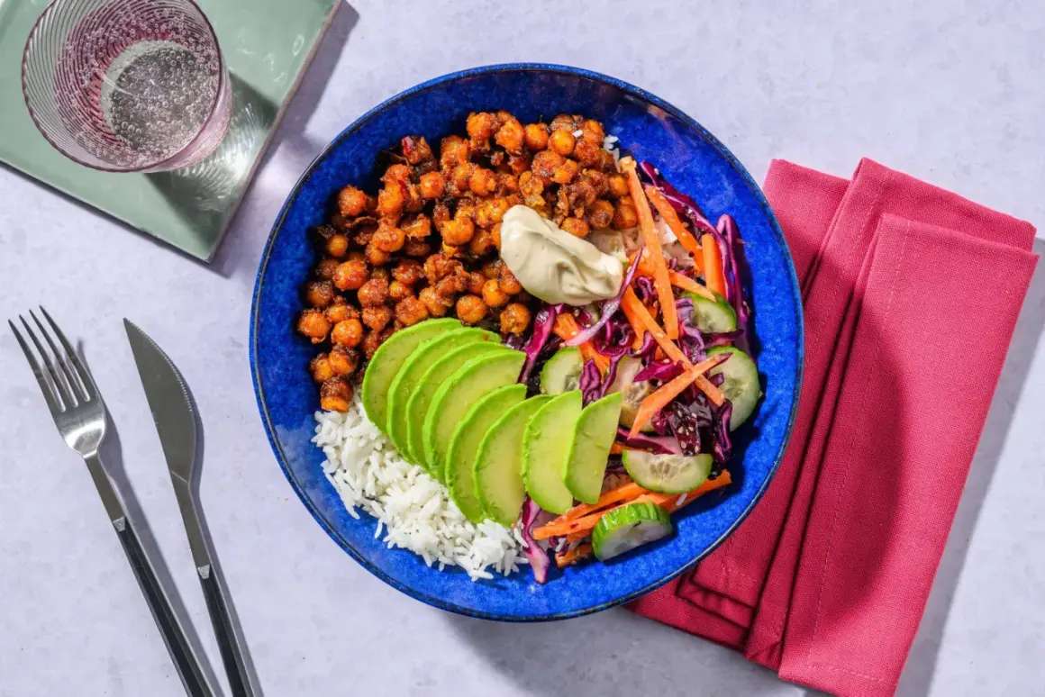 En blå skål med ris, kryddiga kikärtor, avokado, gurka, morot och rödkål. Ett perfekt bowls recept för en snabb och god middag.