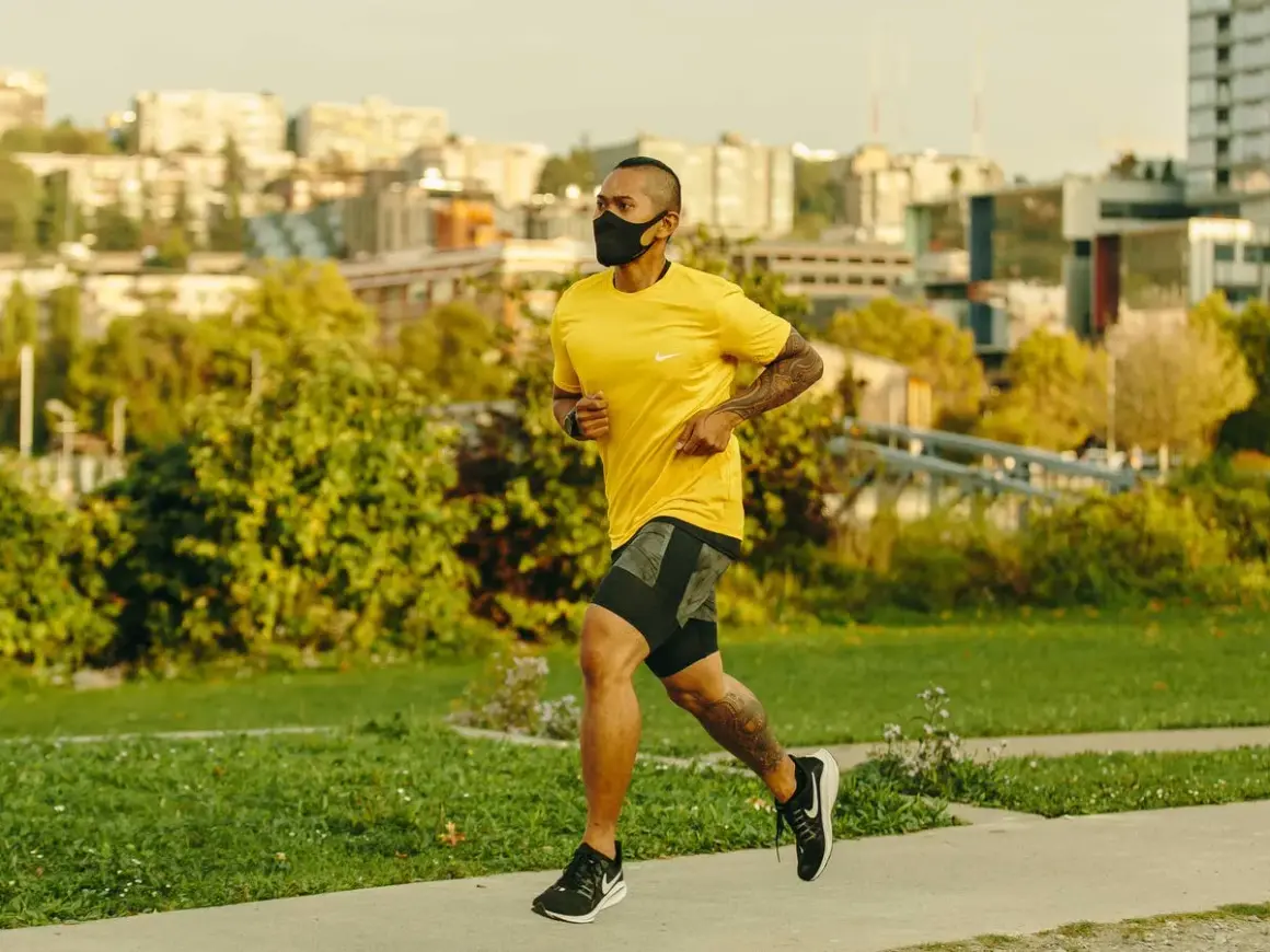 Man running with oxygen mask on a path, city skyline in background.