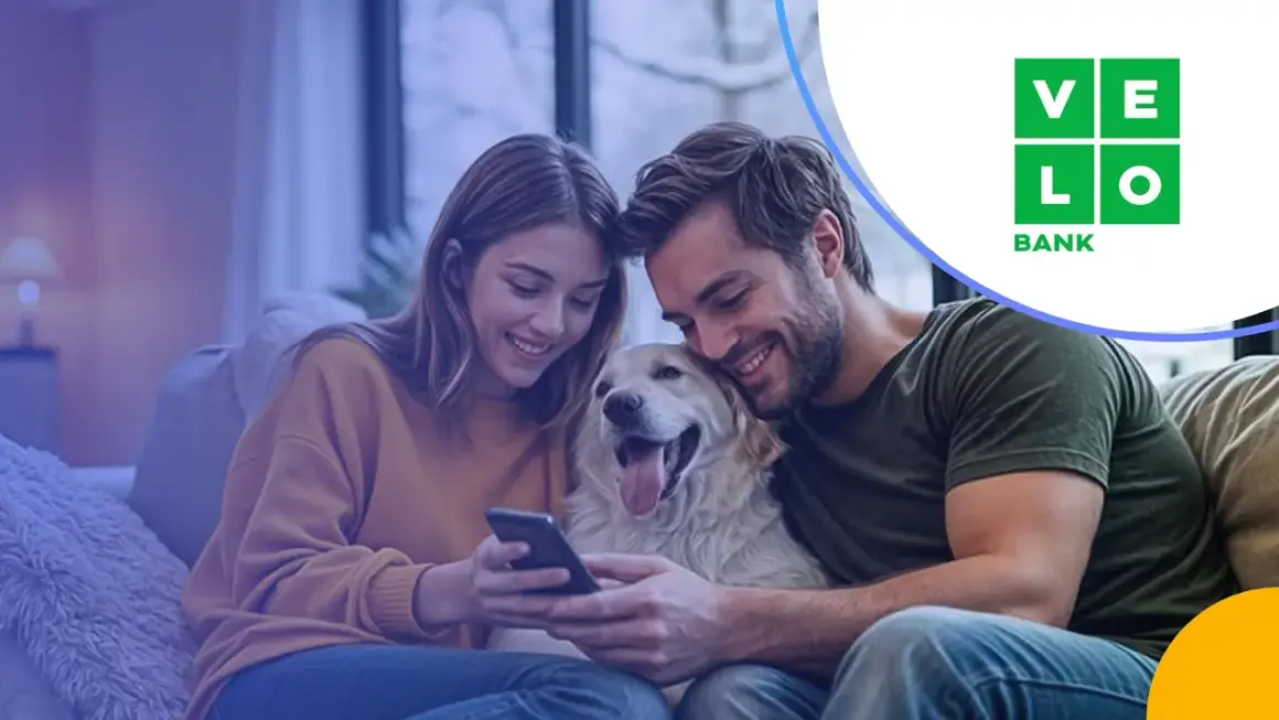 Szczęśliwa para z psem przegląda ofertę velo bank kredyt hipoteczny na telefonie.