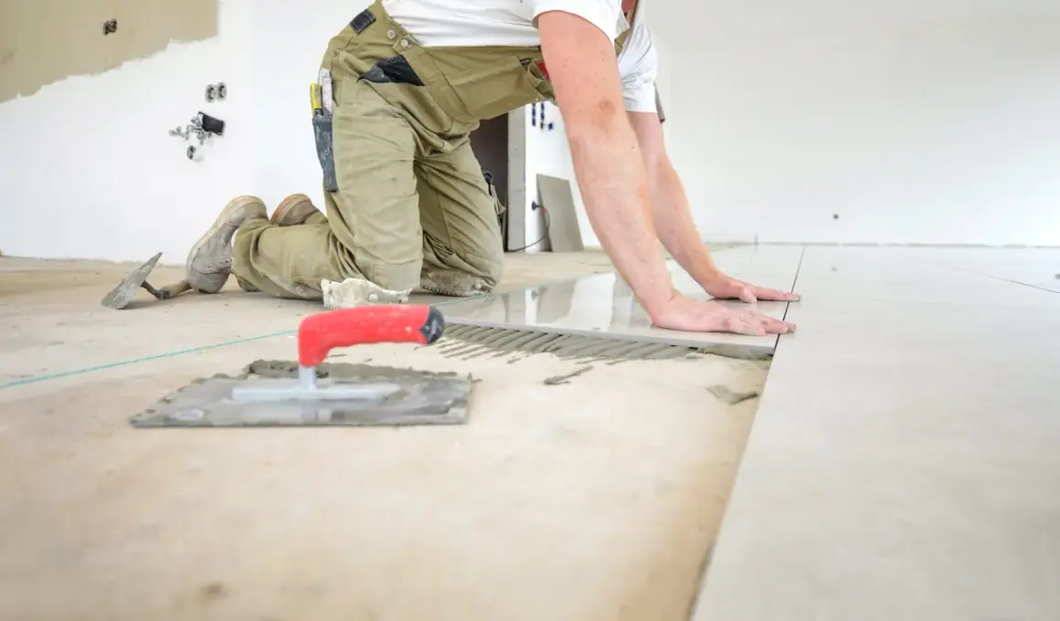 Pose d'un carrelage au sol, le carreleur ajuste la pose pour une épaisseur parfaite. Outils de pose à proximité.