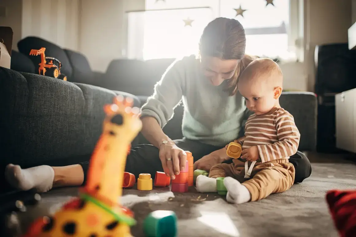 Mama i 7-miesięczne dziecko bawią się kolorowymi klockami na dywanie. Radość i nauka przez zabawę.