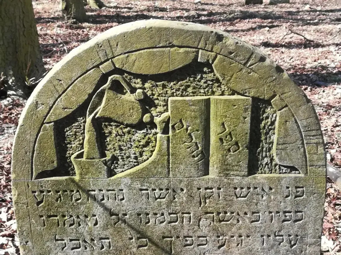 Kamienie na pomniku przedstawiają dzbanek i księgę, symbolizując mądrość i pracę.