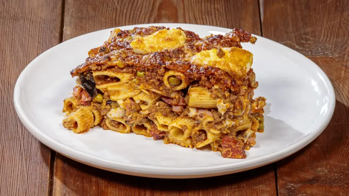 Porzione di pasta ncasciata ricca e saporita, con rigatoni, ragù, uova e verdure, servita su un piatto bianco.