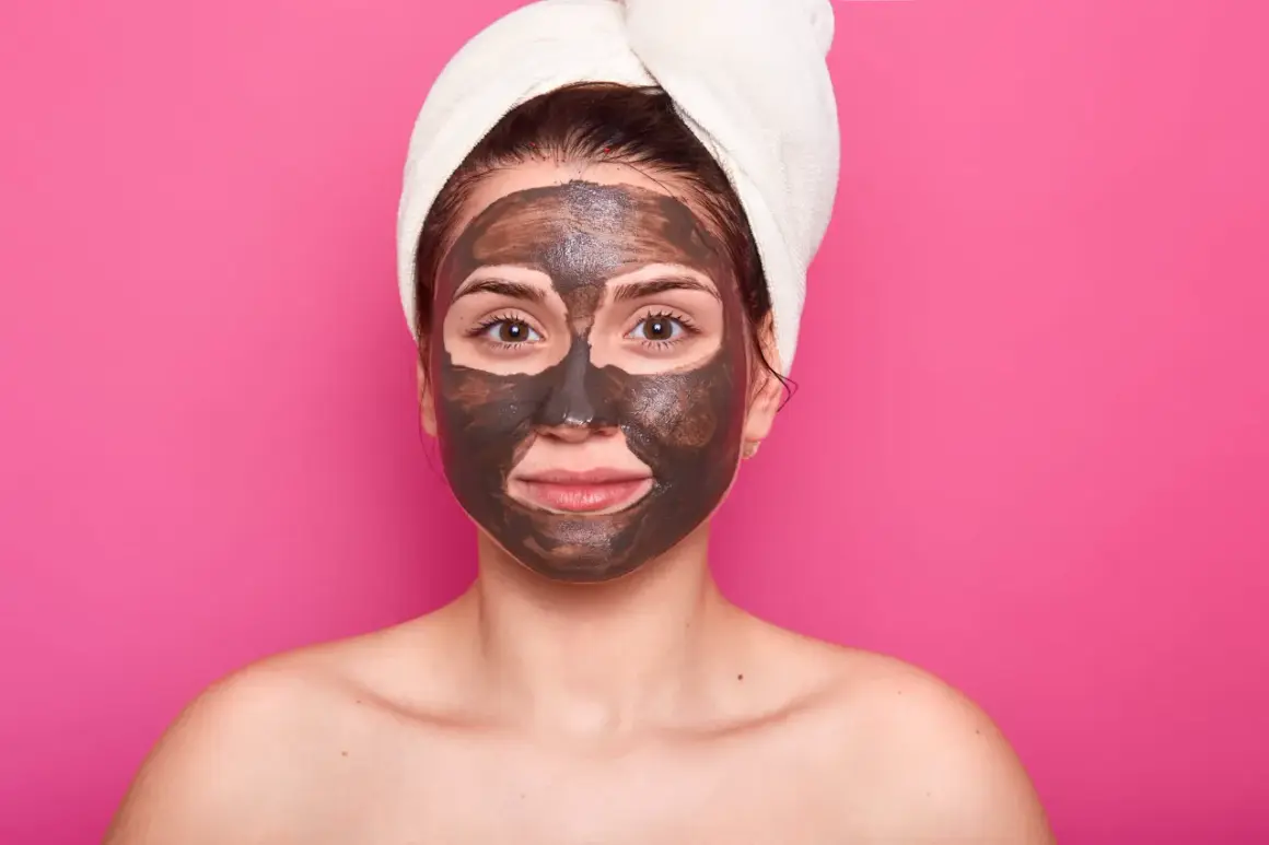 Una mujer con una toalla en la cabeza y una mascarilla de barro en la cara cansada, lista para un tratamiento de spa.