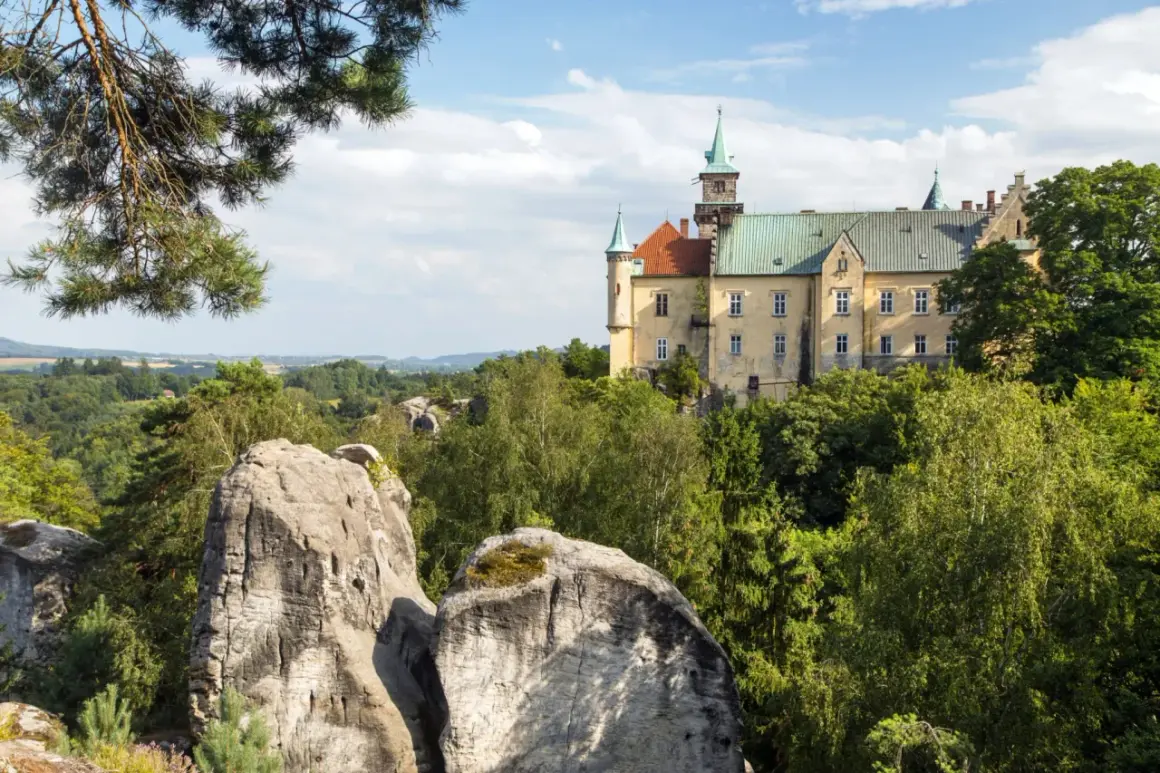 Zamek na skale, otoczony zielenią, to jedna z malowniczych atrakcji w Czechach. Widok na skalne formacje i krajobraz.