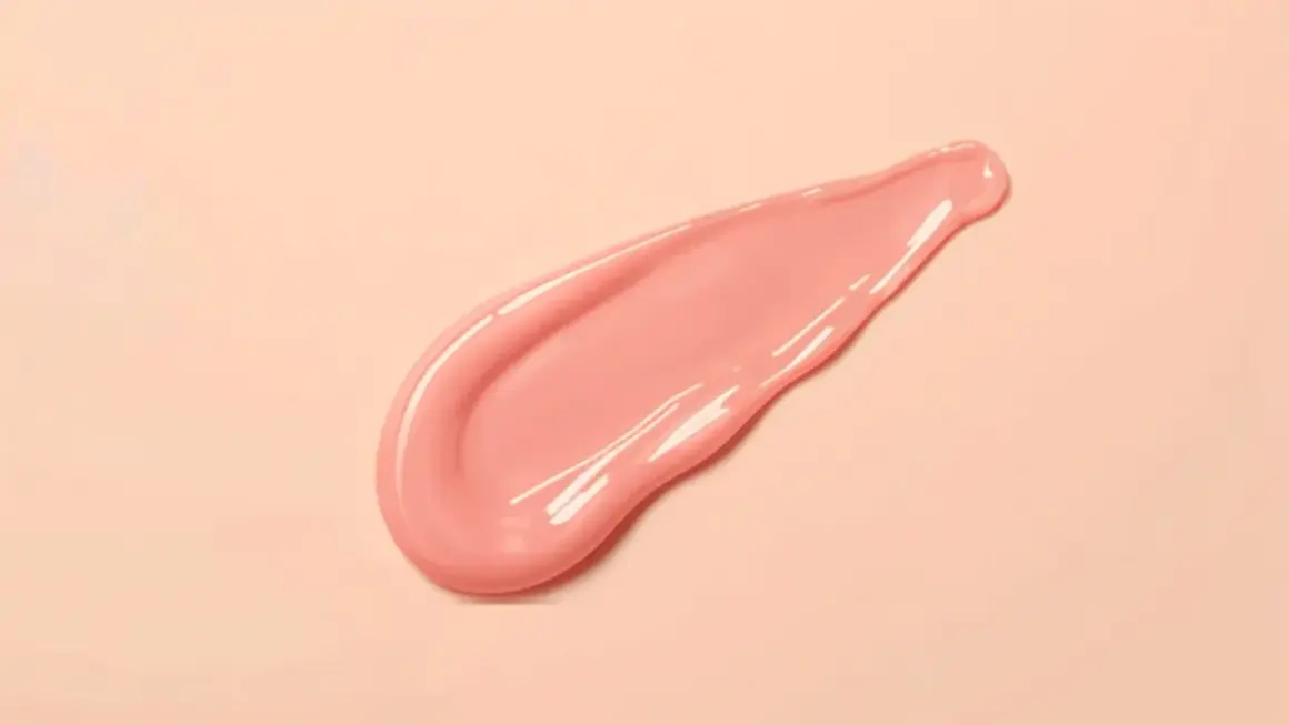 En rosa, glansig sträng av pdrn serum på en ljusrosa bakgrund.