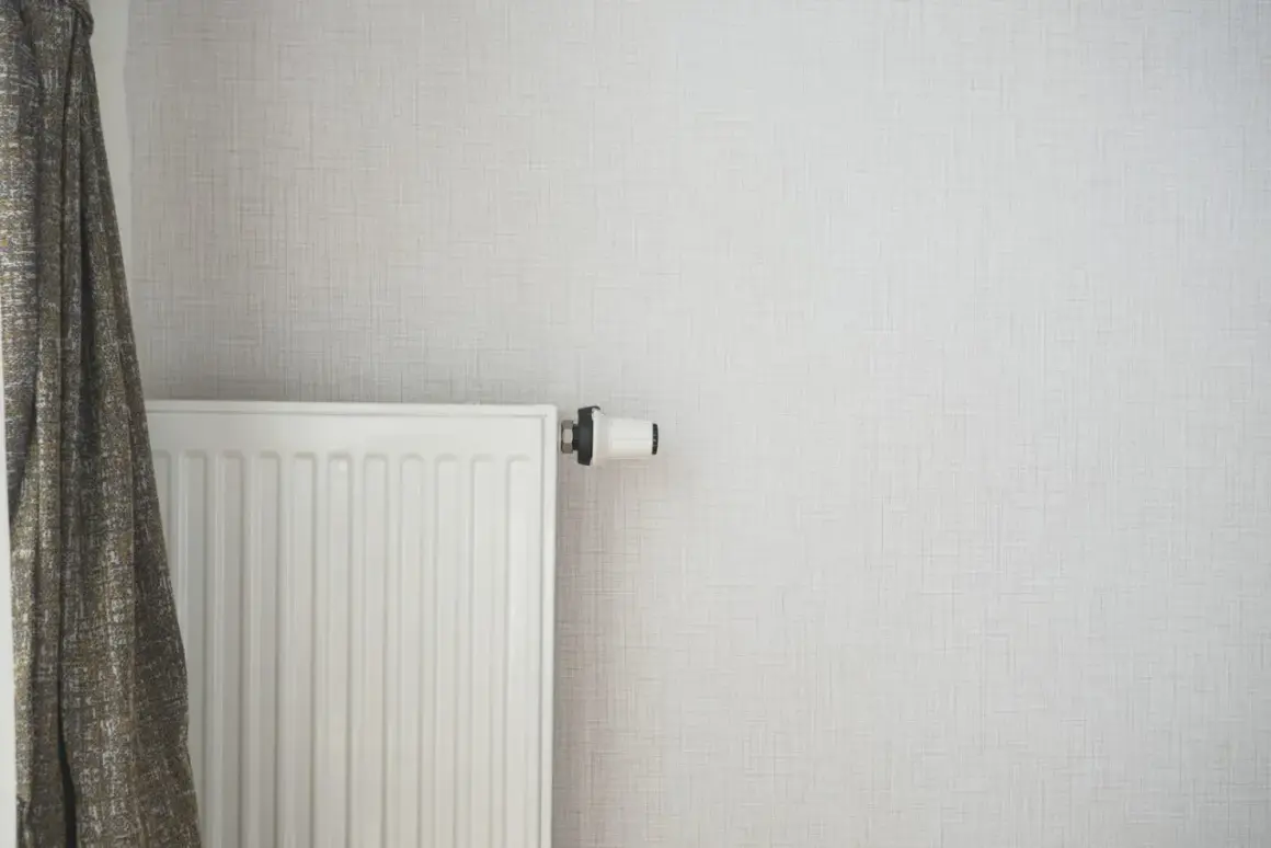 Radiateur blanc moderne, prêt à être alimenté par une pompe à chaleur. Un rideau discret complète la scène.