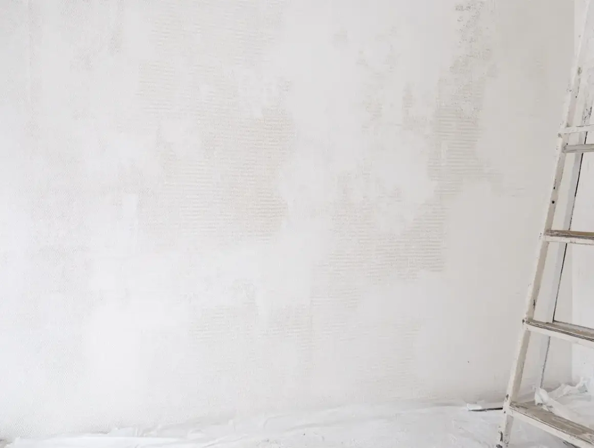 Étape de nettoyage d'un mur blanc jauni, une échelle est visible sur la droite.