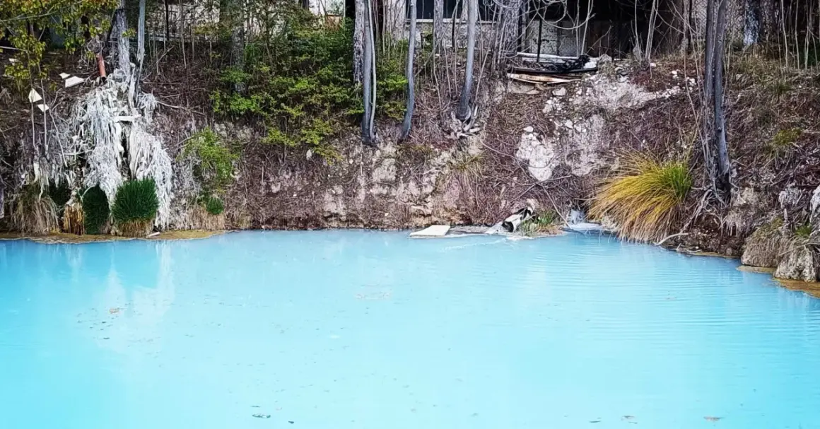 Acque azzurre e torbide delle terme di Cotilia, con vegetazione rigogliosa e rocce erose.