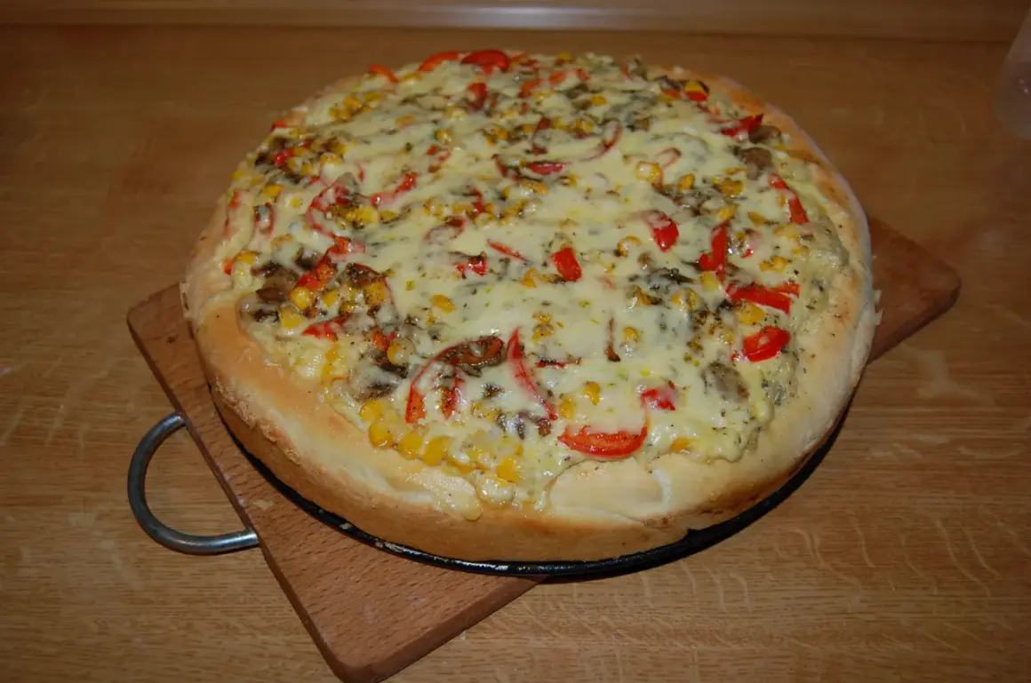 Pizza z kukurydzą, papryką i grzybami, polana obficie białym sosem do pizzy, na drewnianym blacie.