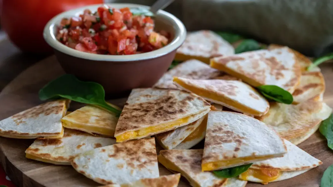 En hög med gyllene, ostiga quesadillas, perfekta för ett snabbt quesadillas recept. Serveras med en skål färsk pico de gallo.