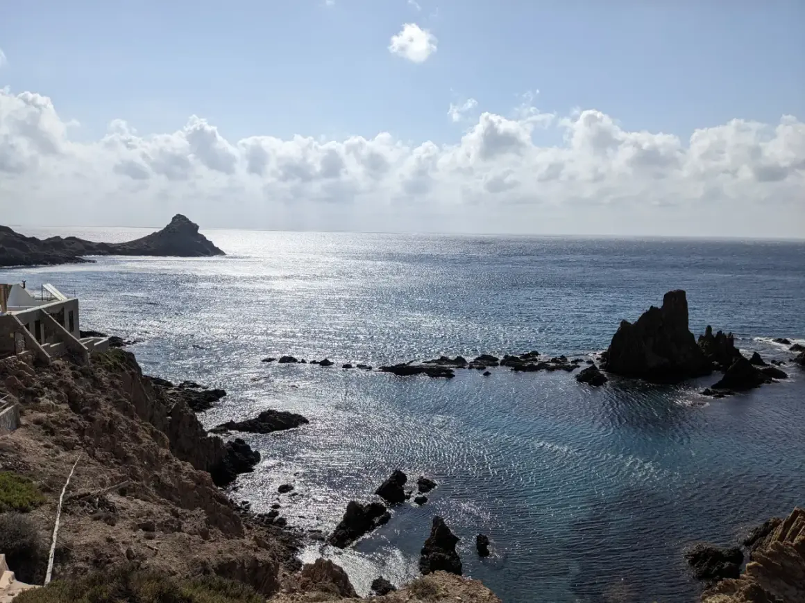 Costa rocosa con formaciones volcánicas emergiendo del mar azul. El arrecife San José se alza majestuoso, reflejando el sol.