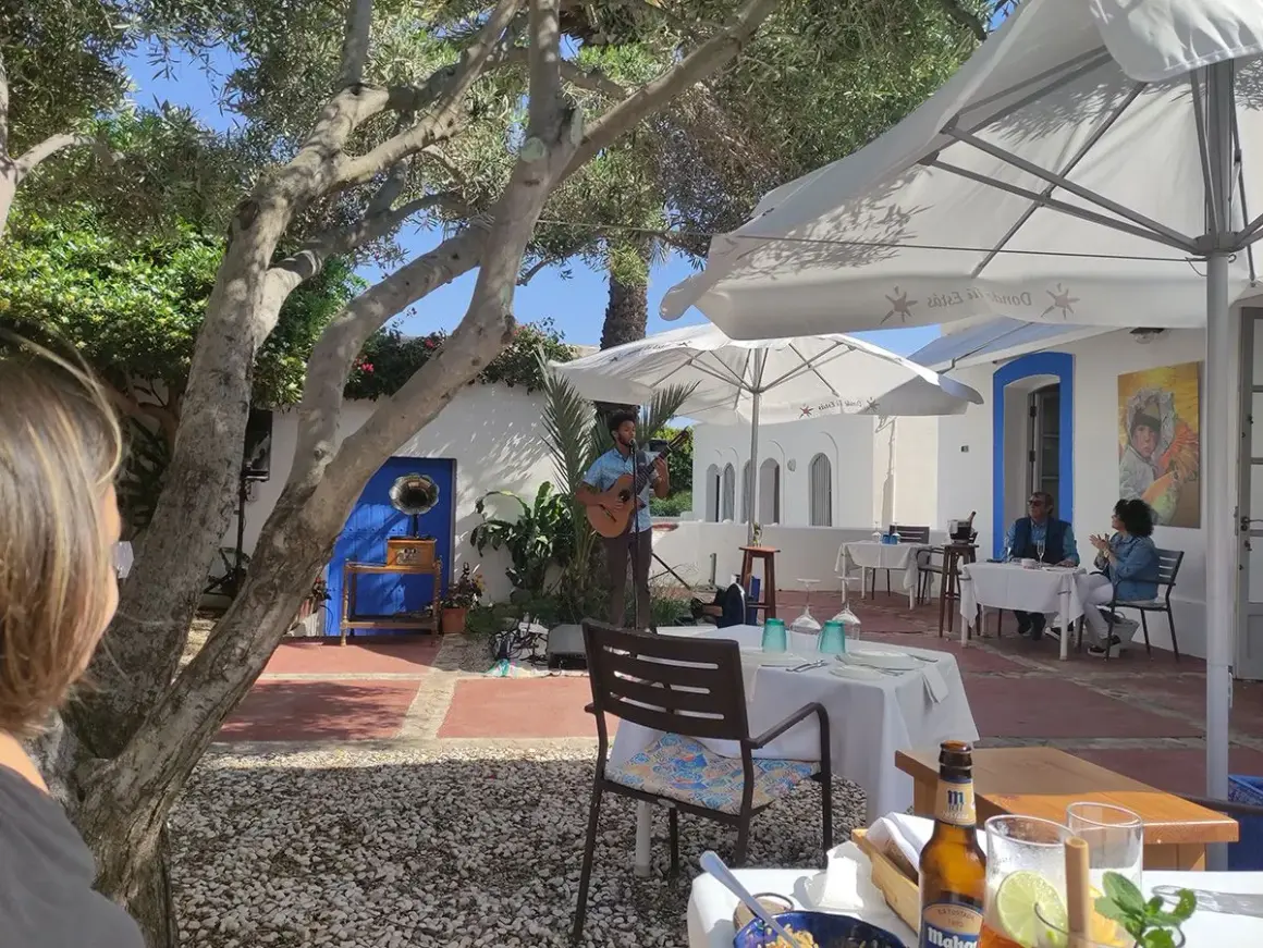 Un músico toca la guitarra en el patio de el pozo de los frailes restaurantes. Mesas puestas bajo sombrillas blancas invitan a disfrutar.