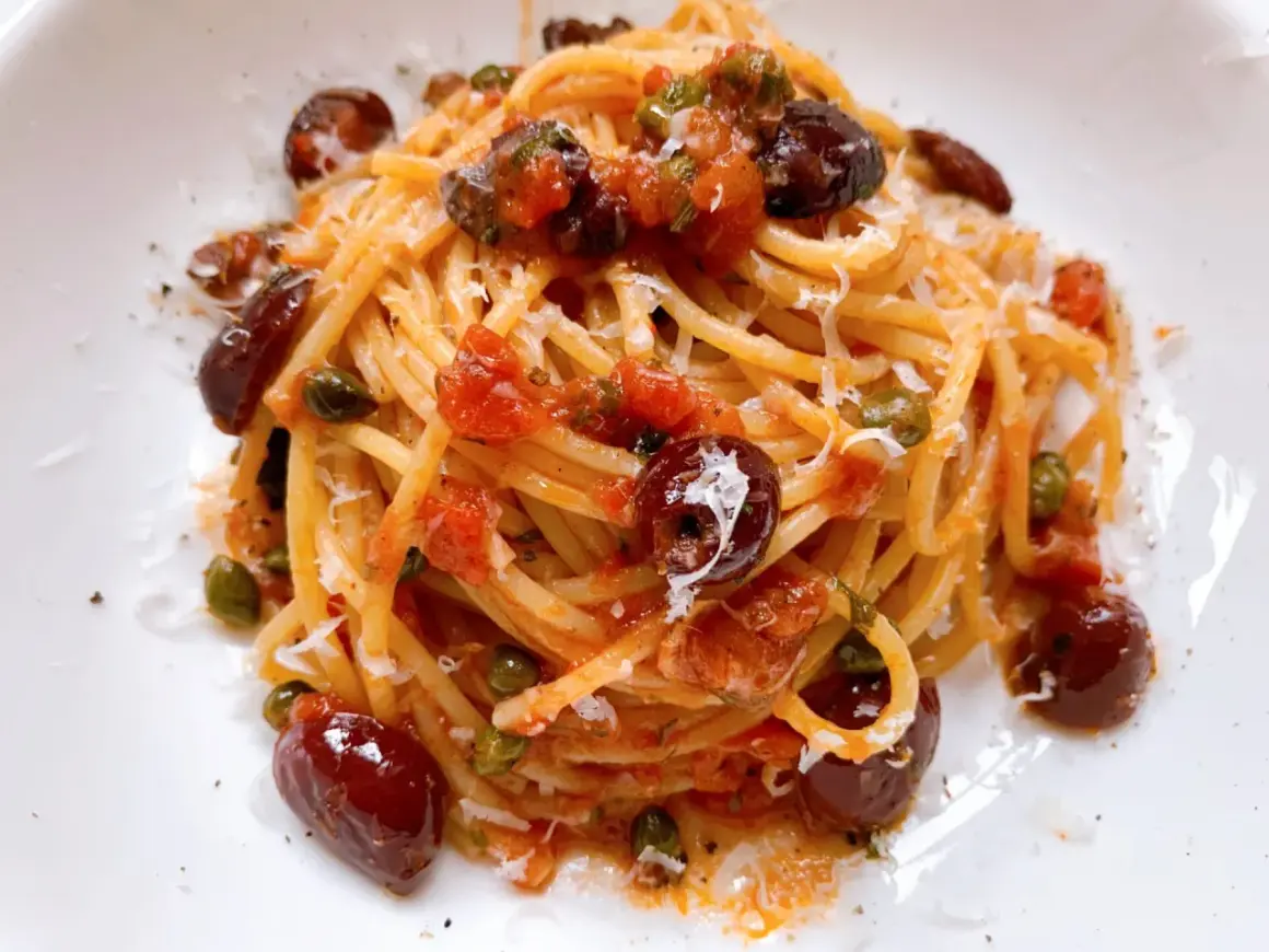 Ein Teller Spaghetti Puttanesca, garniert mit Oliven, Kapern und geriebenem Parmesan.