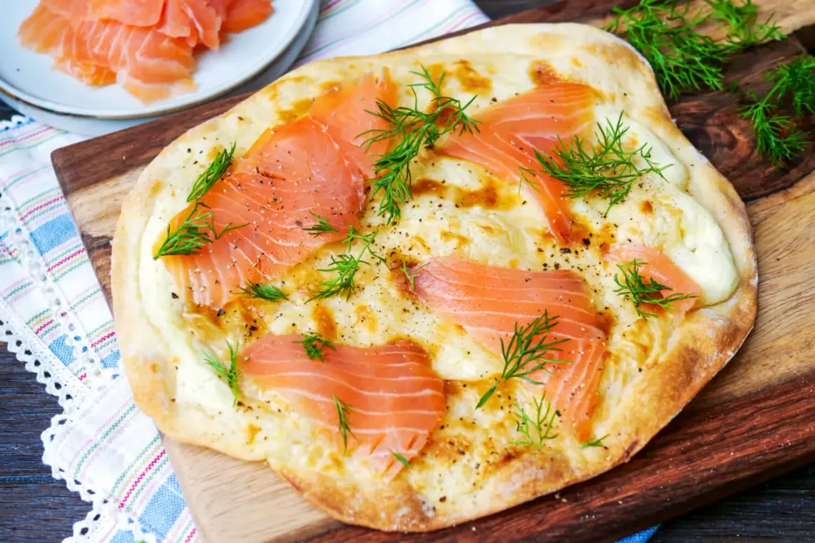 Flammkuchen mit Lachs und Dill, frisch gebacken auf einem Holzbrett.