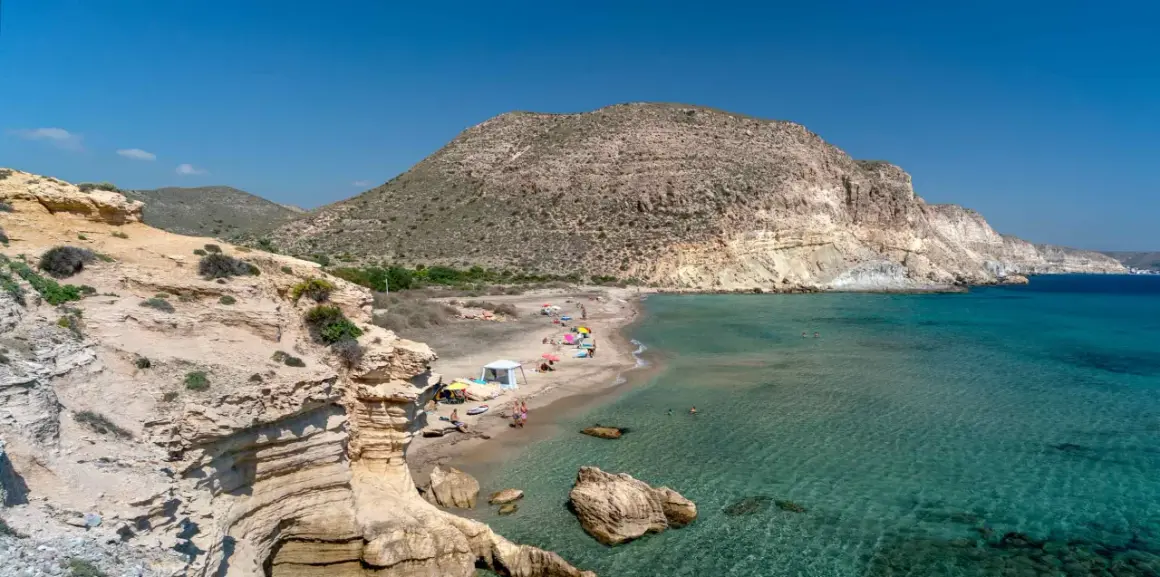 La cala del Peñón Blanco, con su arena dorada y aguas cristalinas, invita a disfrutar del sol bajo un cielo azul.