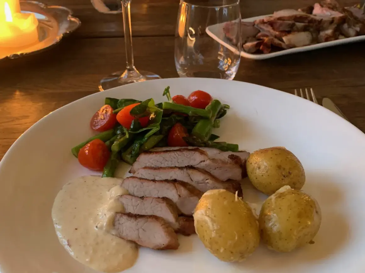 En tallrik med saftigt grillad pluma, serverad med småpotatis, sparris, körsbärstomater och en krämig sås. En härlig måltid!