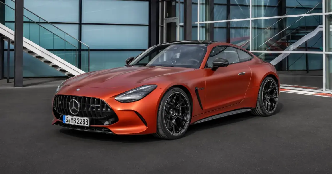 Pomarańczowy Mercedes-AMG GT 63 z czarnymi felgami stoi przed nowoczesnym budynkiem z przeszkloną fasadą i schodami.