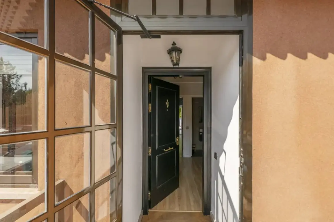 Puerta principal negra abierta, con ventana lateral y luz de porche. Ideas para cerrar un porche con estilo moderno.
