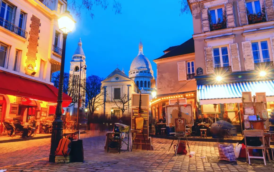 Montmartre di sera, un luogo magico dove uscire a Parigi. Artisti, caffè e la Basilica del Sacro Cuore illuminata.